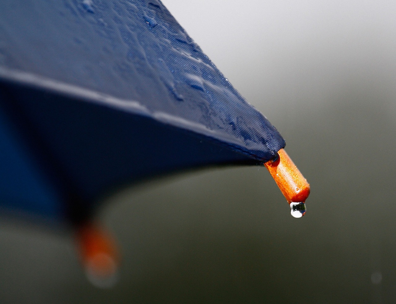 Up-close shot of a blue umbrella with a drip of rain falling off of the wooden frame for Business Umbrella Insurance.