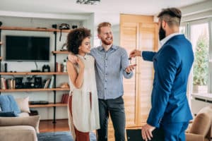 realtor hands a key to a smiling man and woman buying a home