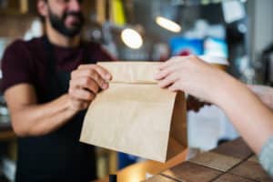 restaurant worker hands takeout bag to customer
