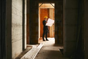 Builder standing in house under construction with building plans
