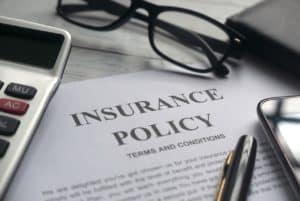 Insurance policy terms information on a desk surrounded by glasses, a pen, a calculator, and a phone.