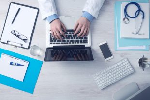 Health Doctor on laptop, stethoscope on top of patient files for Group Health Insurance.