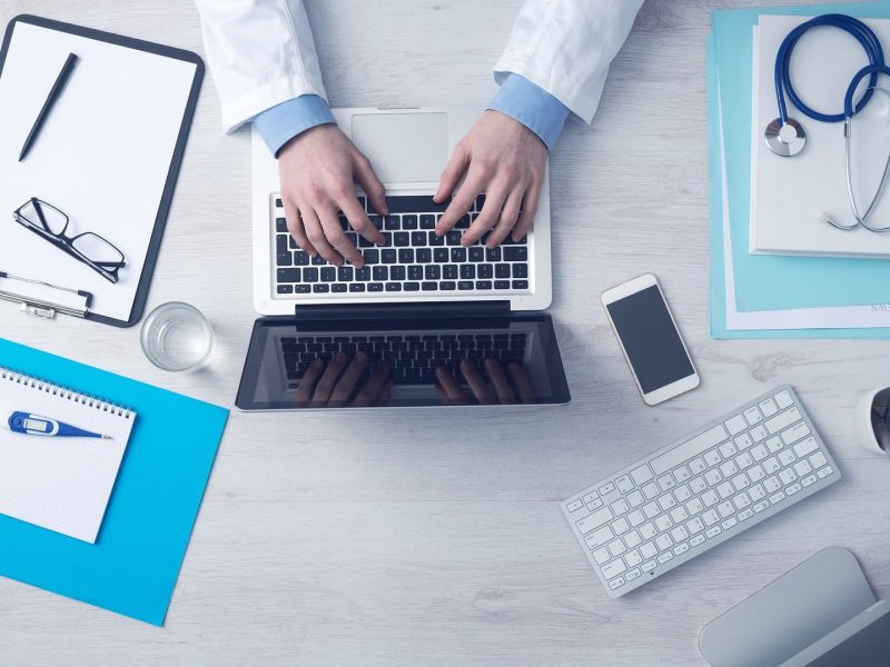 Health Doctor on laptop, stethoscope on top of patient files for Group Health Insurance.