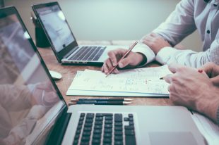 Professional Liability Insurance Business man and colleague reviewing document together with two laptops on desk and pen in hand for Professional Liability Insurance.