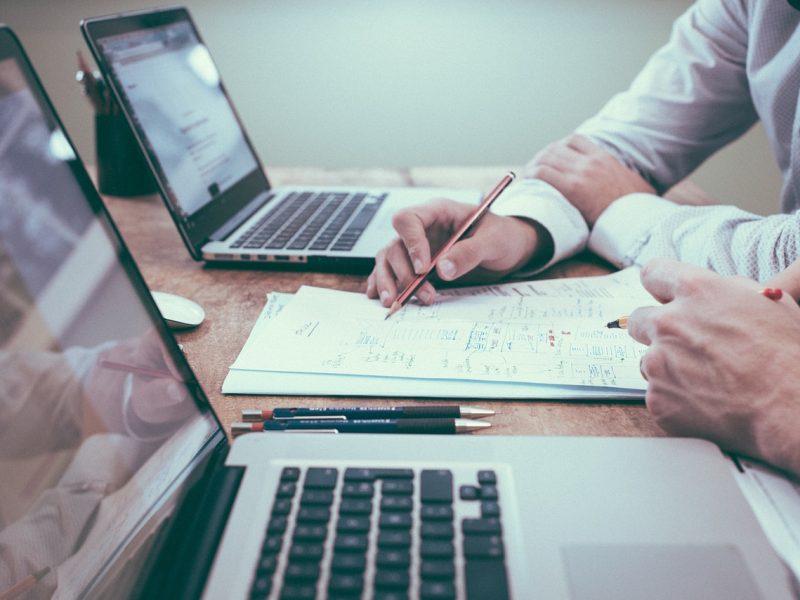 Business man and colleague reviewing document together with two laptops on desk and pen in hand for Professional Liability Insurance.